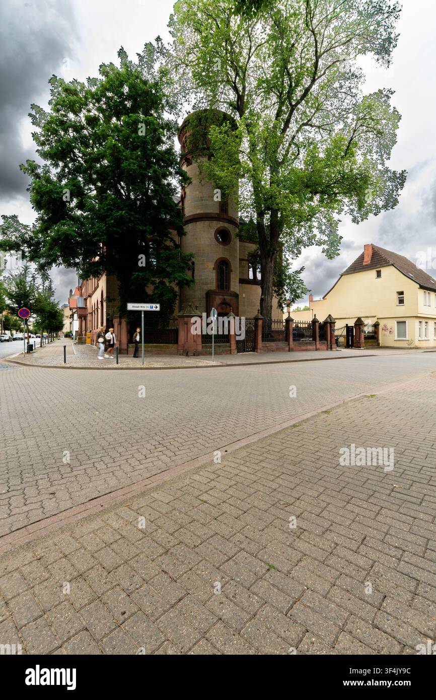 23 luglio 2026, Quedlinburg, Sassonia-Anhalt, Germania: Edificio storico con una torre rotonda e alberi maturi a un angolo di strada vicino al centro storico. Foto Stock