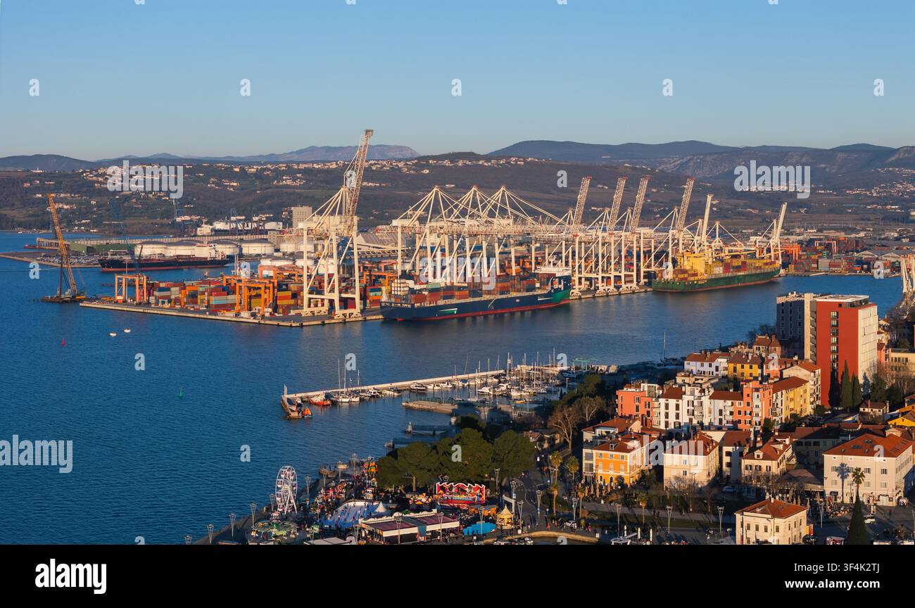 Un porto commerciale affollato con container di merci, gru e barche lungo il corso d'acqua. Foto Stock
