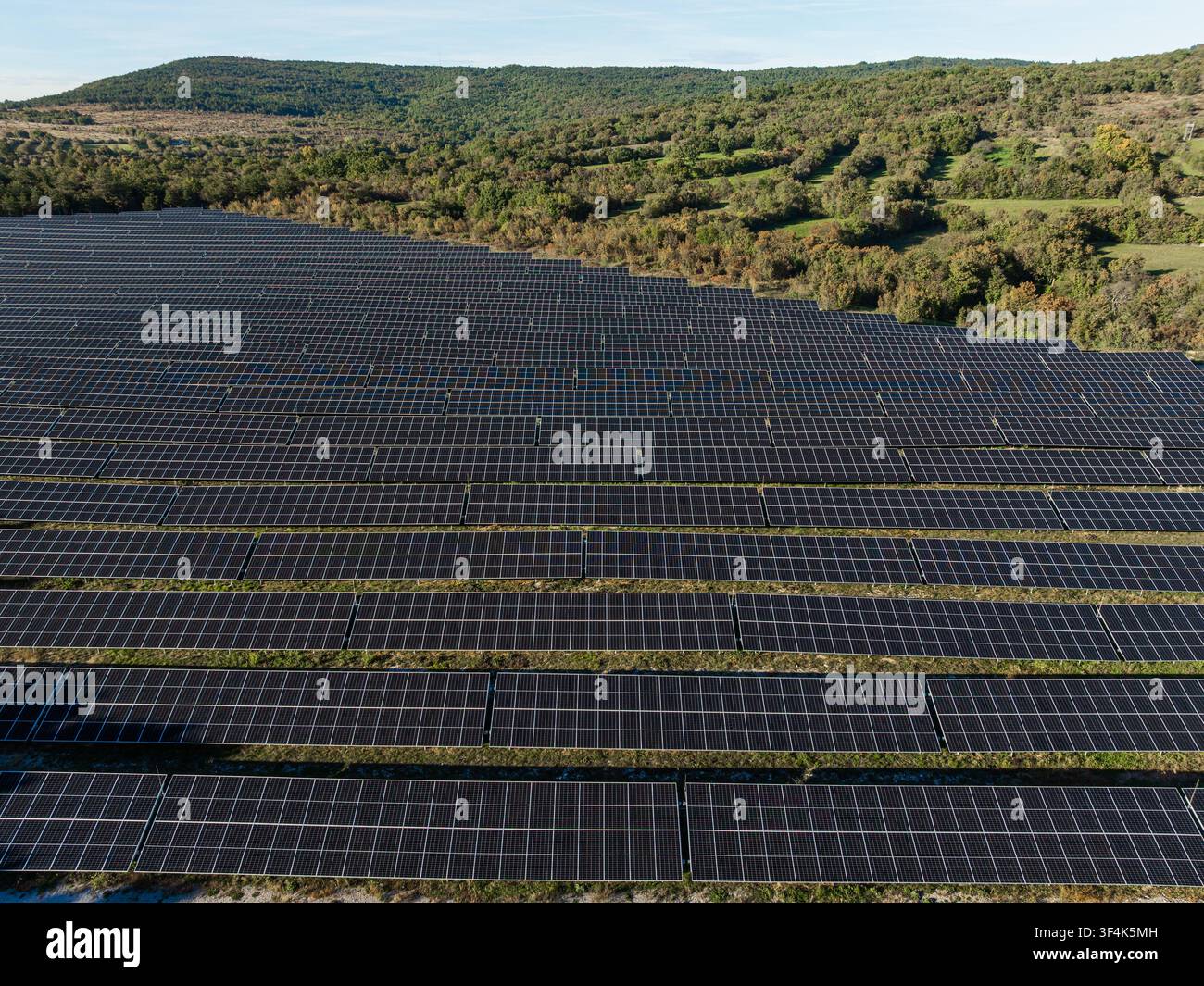 Farm solare con molti pannelli fotovoltaici genera elettricità pulita in un contesto rurale sotto un cielo sereno. Questo promuove l'uso di energia rinnovabile. Foto Stock