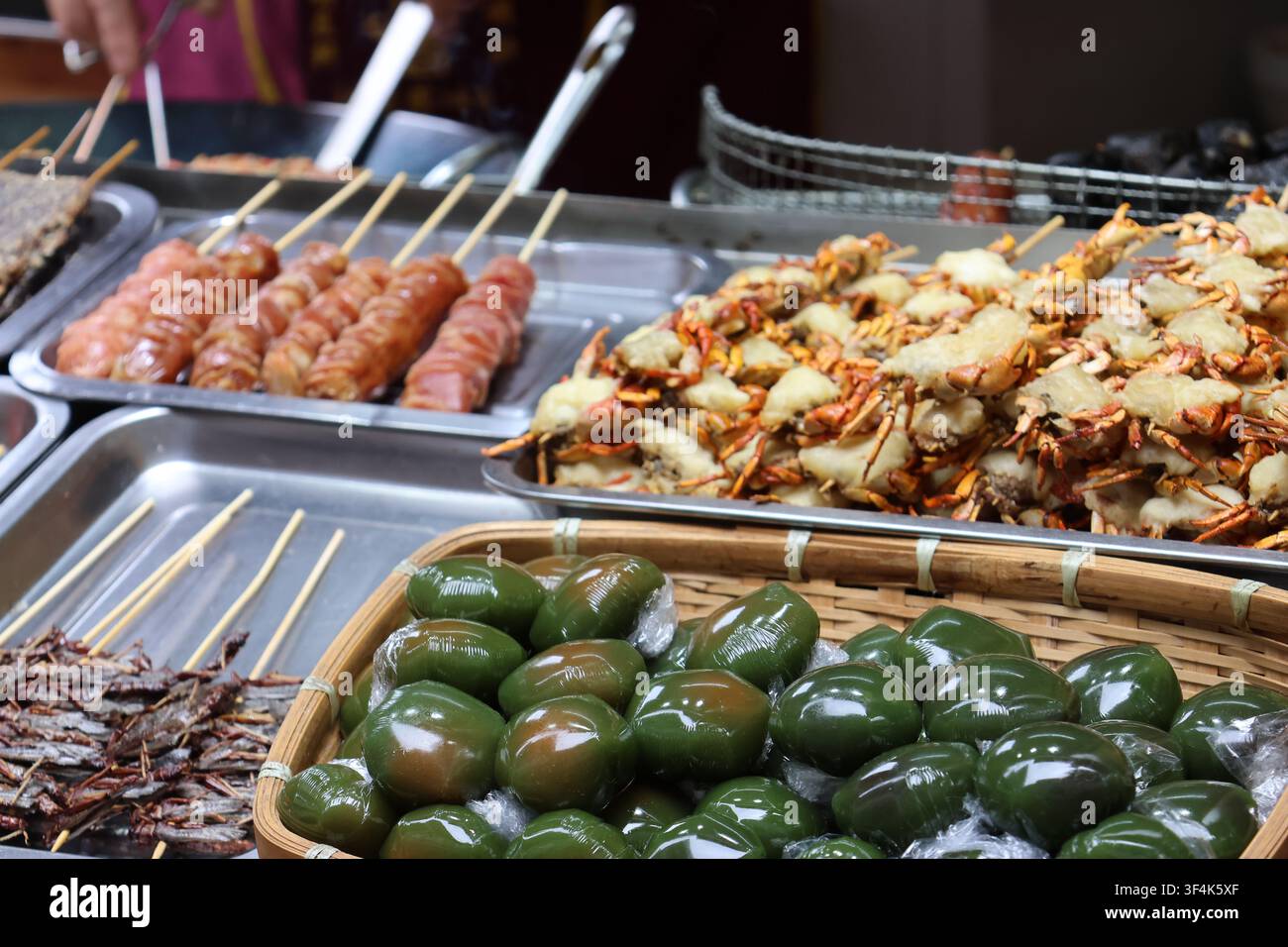 Tortini di riso glutinoso al mughetto, granchi dalle chele molli fritti, cavallette fritte e salsiccia esposti in un mercato di strada della contea di Fenghuang, Hunan, Cina Foto Stock