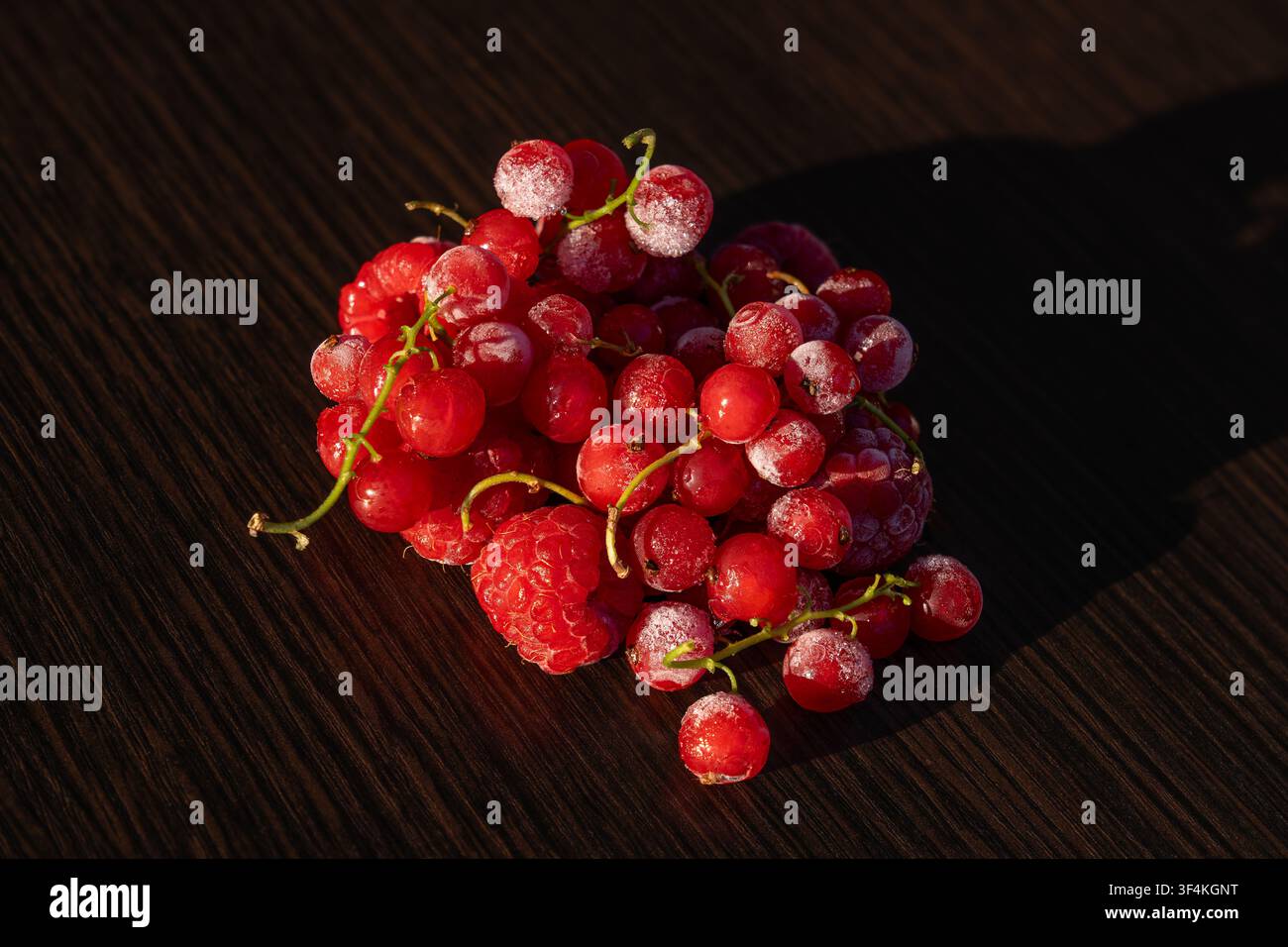 Mucchio di ribes rossi e lamponi congelati con brina su tavolo di legno scuro Foto Stock