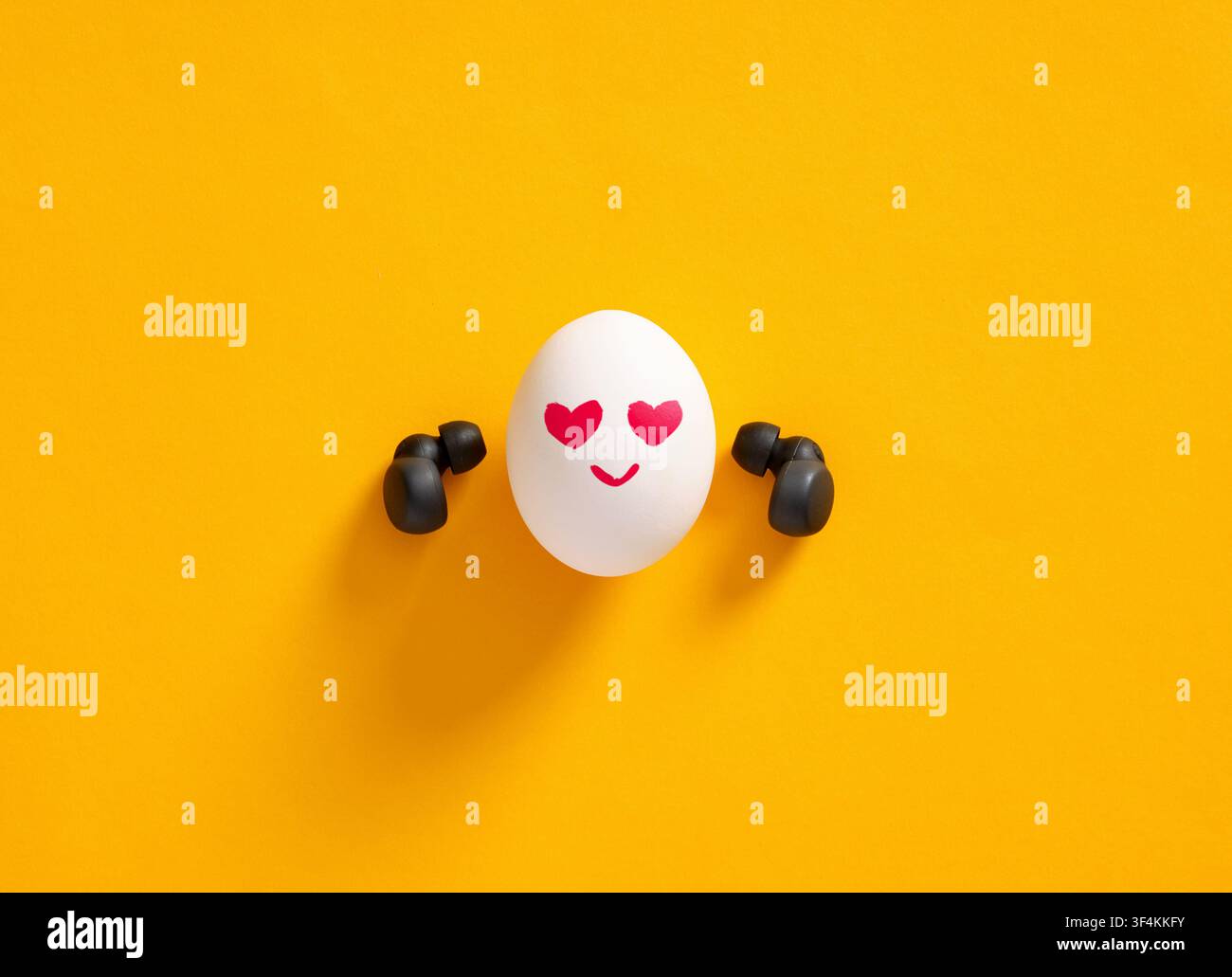 Personaggio a forma di uovo con auricolari senza fili, che esprime l'amore per la musica o ascolta una canzone d'amore romantica con occhi a forma di cuore e un sorriso felice su uno sfondo giallo Foto Stock