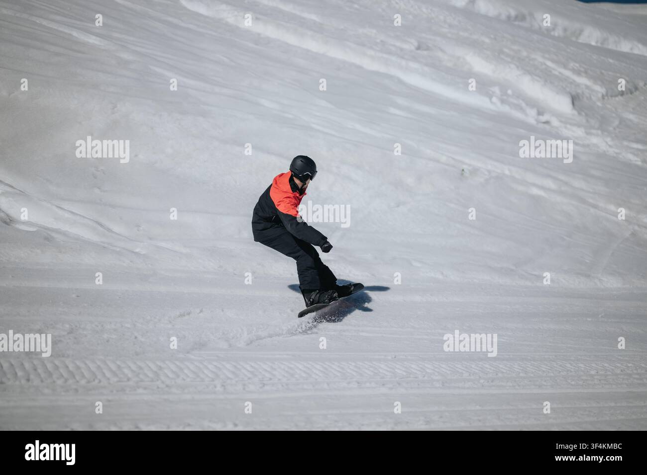 Snowboarder che scivola lungo una pista innevata ben preparata con una giacca invernale luminosa in una giornata serena Foto Stock