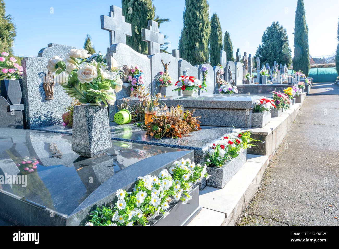 Lapidi di granito e decorazioni floreali che segnano i luoghi di sepoltura in un cimitero tranquillo Foto Stock
