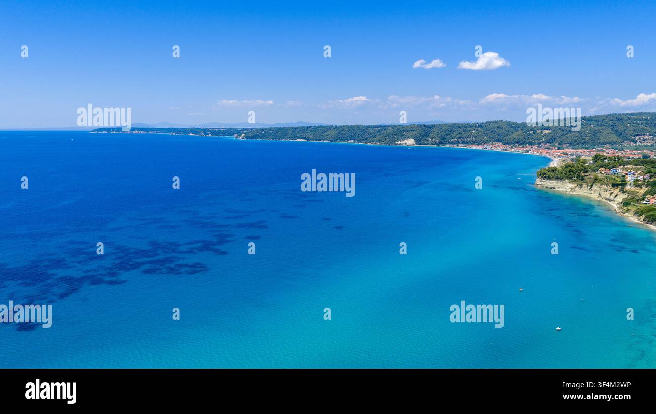 Spiaggia di Possidi, Grecia, 11 luglio 2026. Un mare turchese chiaro si estende accanto alla costa boschiva di Possidi, con motivi di acqua poco profonda e un distante Foto Stock