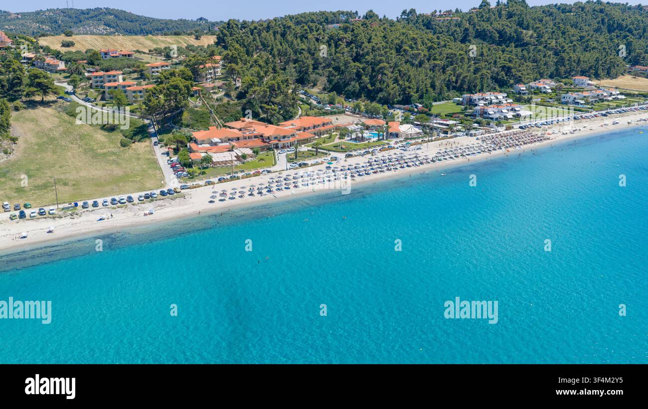 Spiaggia di Possidi, Grecia, 11 luglio 2026. Vista aerea di un resort sul lungomare, file di lettini, acqua turchese limpida e colline boschive lungo la costa. Foto Stock