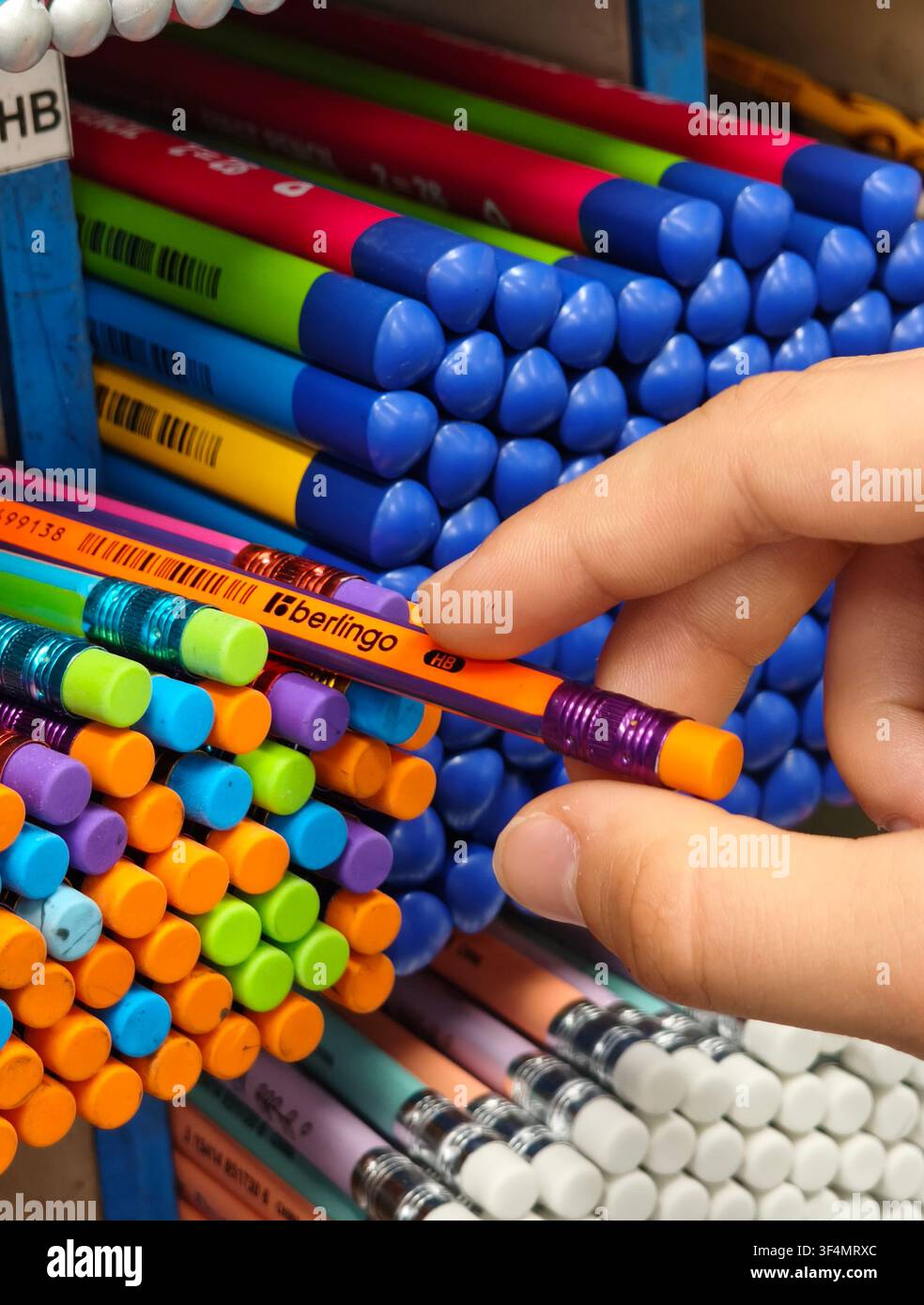 Una mano che sceglie una matita colorata Berlingo HB di grafite con gomma da un'esposizione in negozio, rappresentando creatività, educazione e preparazione. - Immagine stock catturata con smartphone