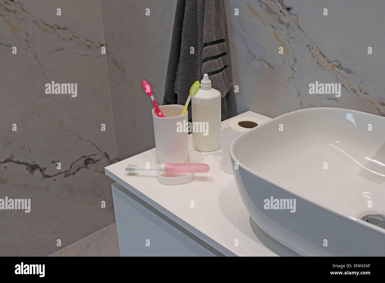 Topo da bagno moderno con lavandino, spazzolini da denti, dentifricio, erogatore di sapone e carta igienica. Interno pulito con articoli di igiene personale quotidiani. Foto Stock