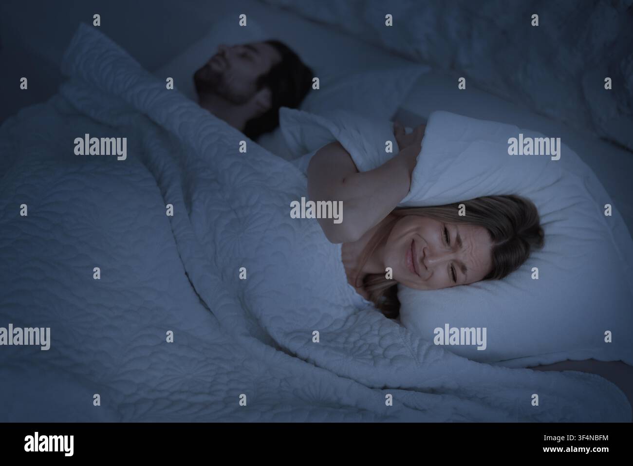 Donna che si copre le orecchie a letto mentre il partner dorme, concetto di interruzione del sonno Foto Stock
