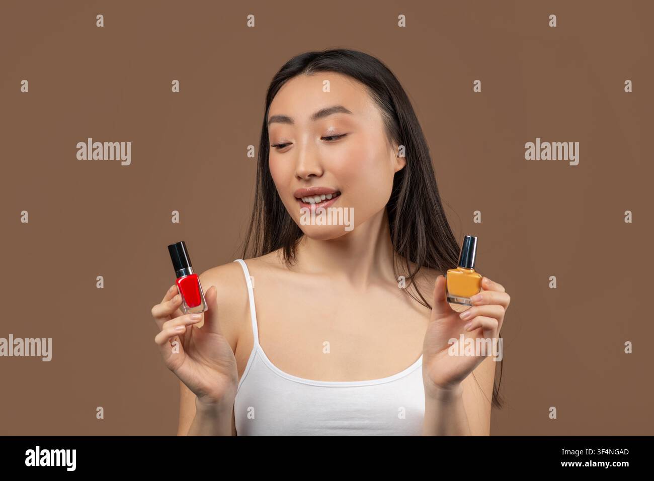 Giovane donna asiatica sorridente che tiene bottiglie di smalto per unghie rosso e giallo, concetto di bellezza Foto Stock