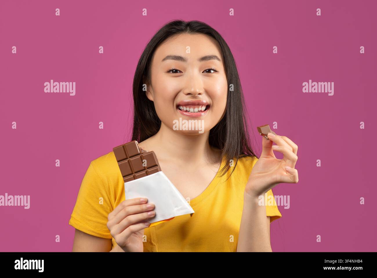 Donna asiatica felice sorridente, tiene una barretta e un pezzo di cioccolato, ambientazione in studio, concetto di spuntino Foto Stock