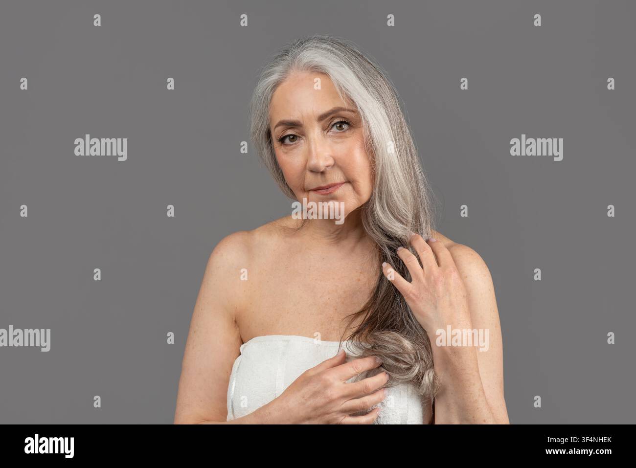 Donna anziana con capelli grigi che tiene capelli lunghi, concetto di bellezza naturale Foto Stock