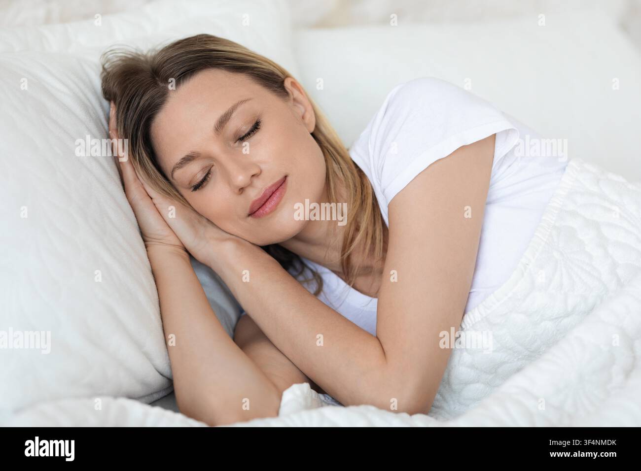 Giovane donna che dorme comodamente a letto con cuscini morbidi e una coperta calda Foto Stock
