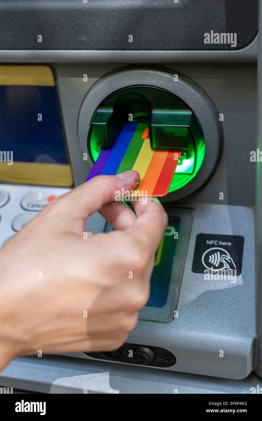 Persona che inserisce una carta di credito arcobaleno in un bancomat Foto Stock