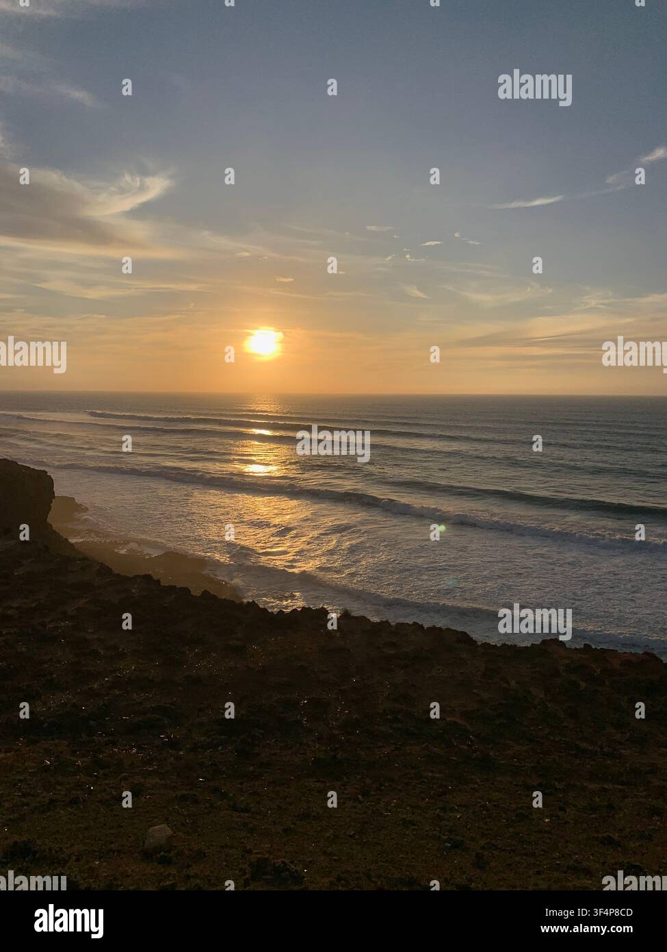 Tramonto dorato sull'oceano con increspature delle onde e una drammatica costa rocciosa - Immagine stock catturata con smartphone