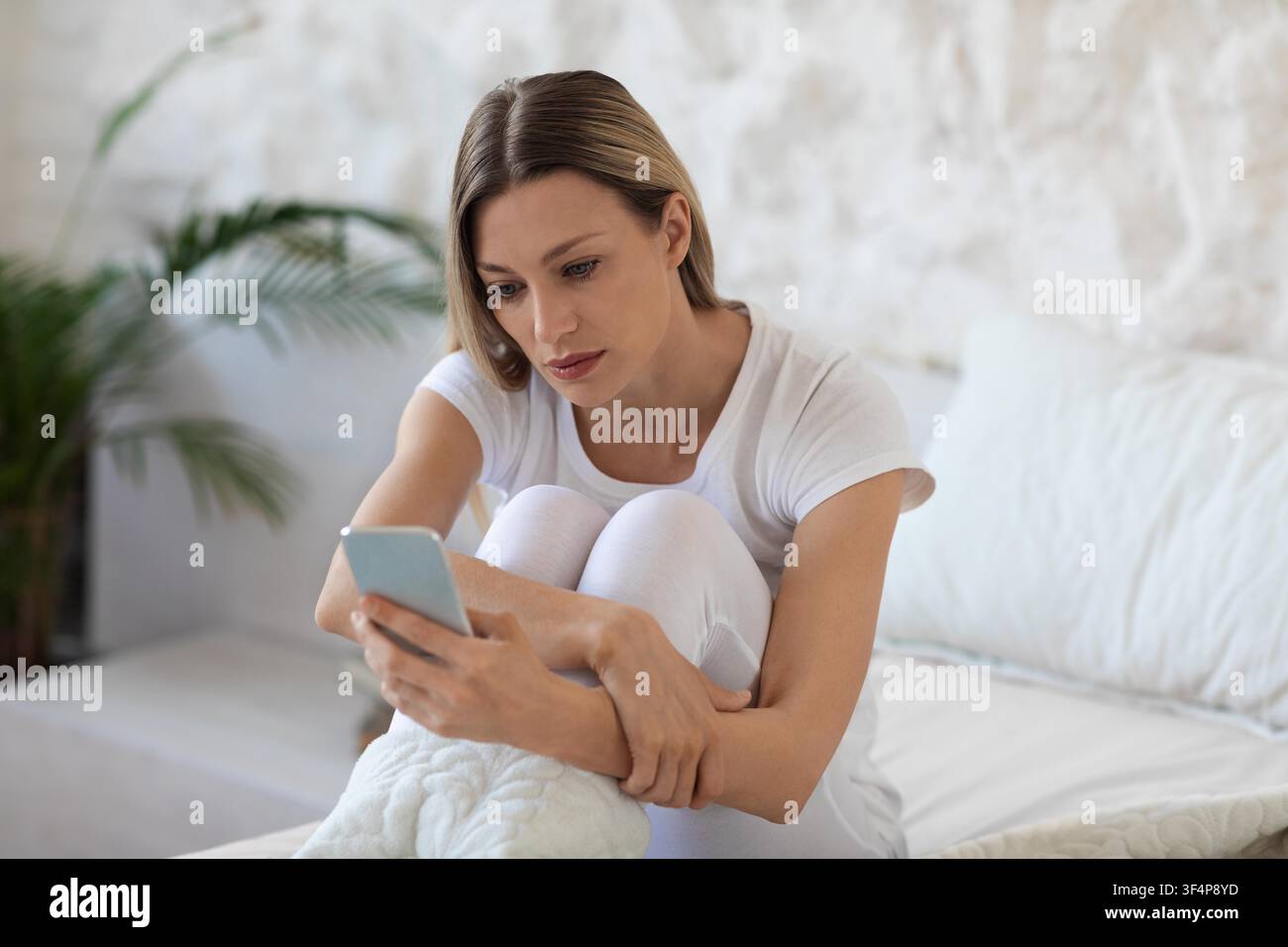 Giovane donna caucasica concentrata che legge messaggi sullo smartphone a casa, rilassandosi Foto Stock