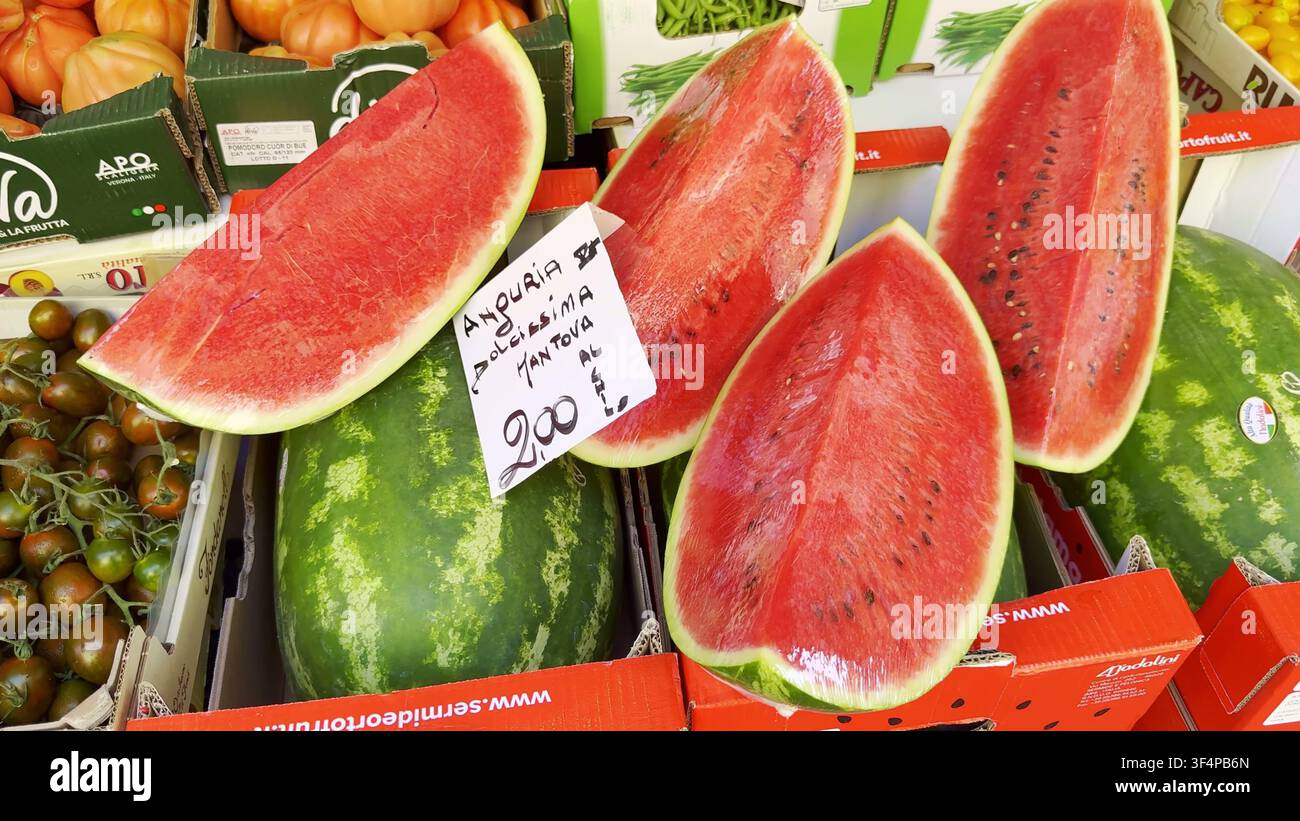 MILANO, ITALIA - 15 GIUGNO 2024: Anguria rossa fresca tagliata a metà e a fette avvolta nella pellicola trasparente con un cartellino del prezzo esposto in un mercato della frutta a Milano, Ital Foto Stock