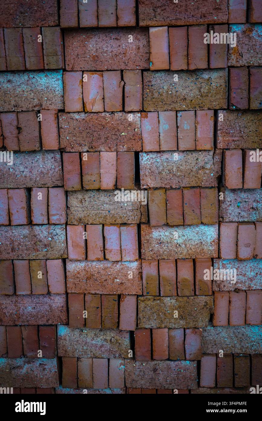Un primo piano verticale a tutta cornice mostra un muro di mattoni rossi rettangolari impilati uniformemente, alcuni dei quali presentano superfici ruvide e consumate con bianchi e Foto Stock