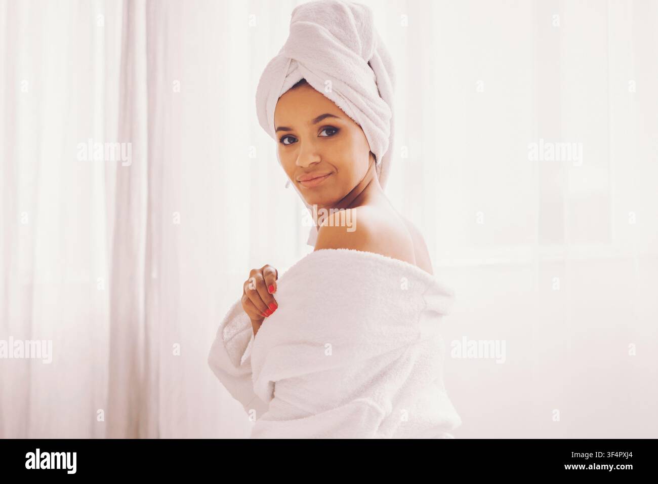Giovane donna con asciugamano che sorride e si rilassa a casa dopo la doccia, concetto di cura personale Foto Stock
