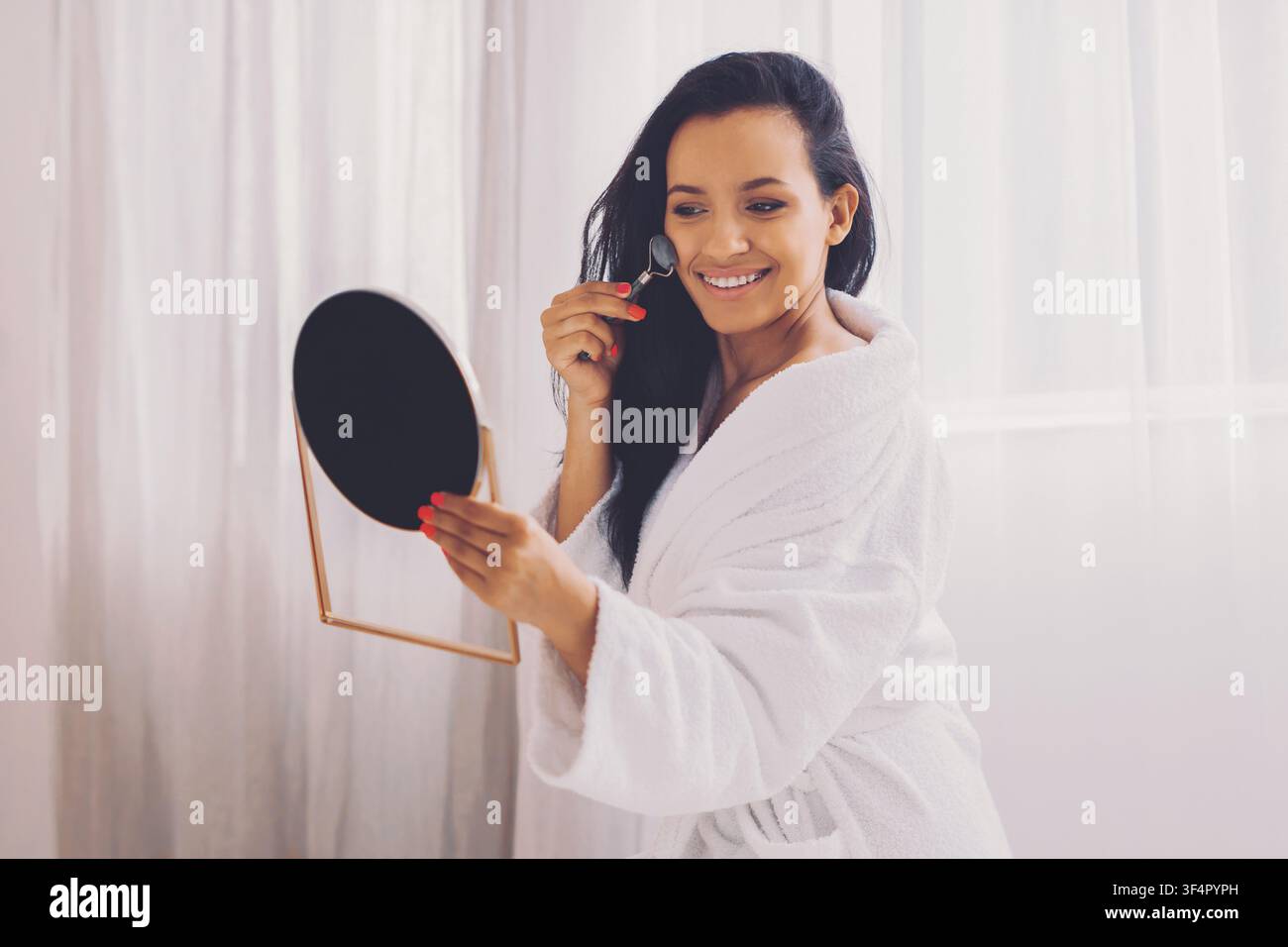 Donna felice che applica crema viso davanti allo specchio a casa, concetto di cura personale Foto Stock
