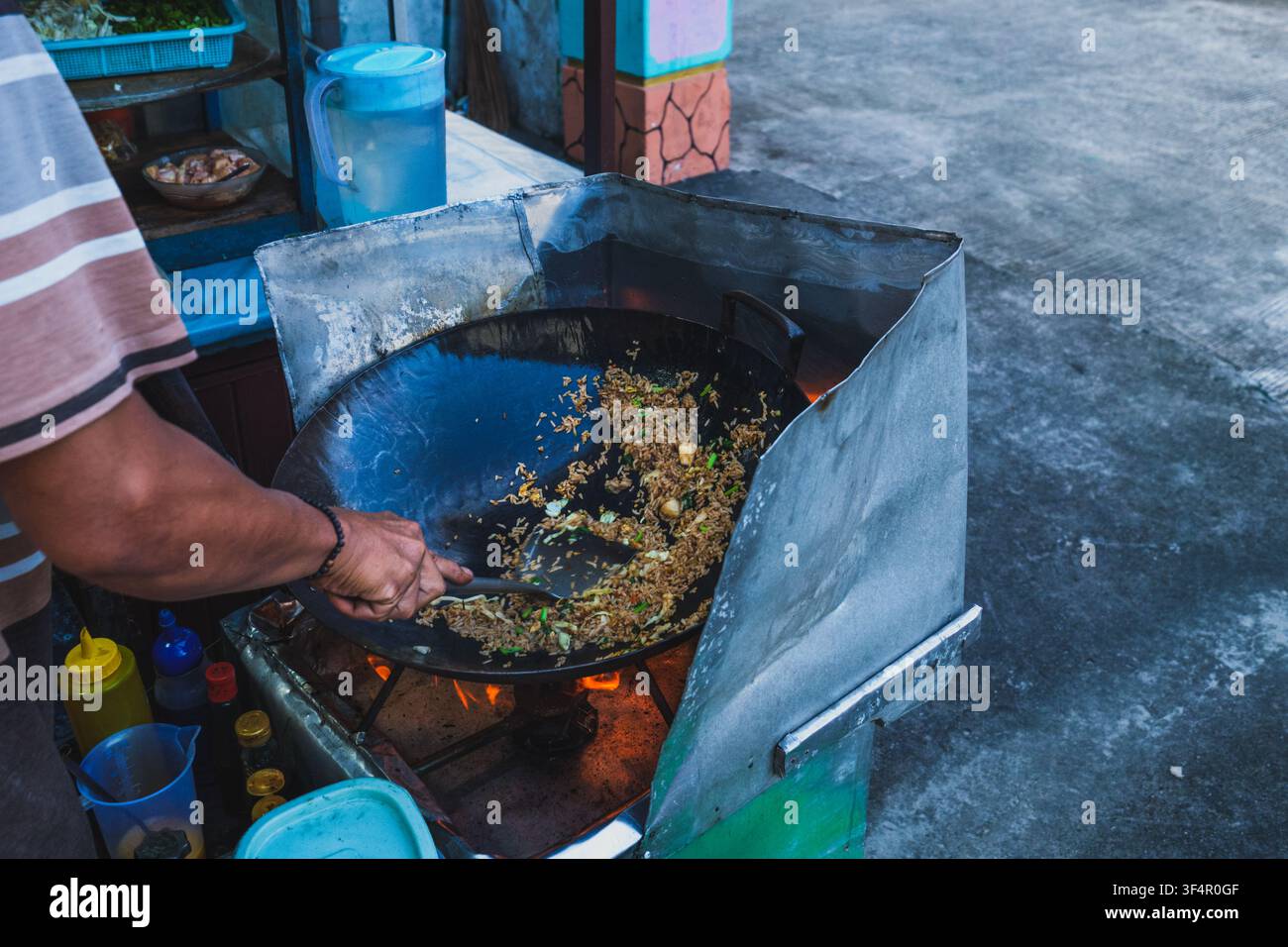Un primo piano di un venditore di street food indonesiano che usa una spatola di metallo per saltare riso stagionato (nasi goreng) in un grande wok caldo. Foto Stock