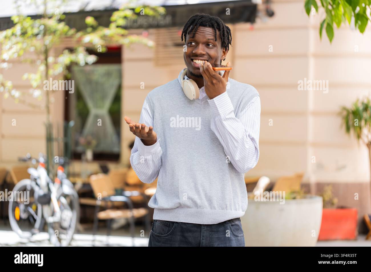 Giovane uomo afroamericano che parla al telefono mentre cammina per una strada cittadina, spiegando tramite vivavoce. Turista nero che gesticola all'aperto durante una chiamata vocale condividendo indicazioni o consigli di viaggio in città Foto Stock