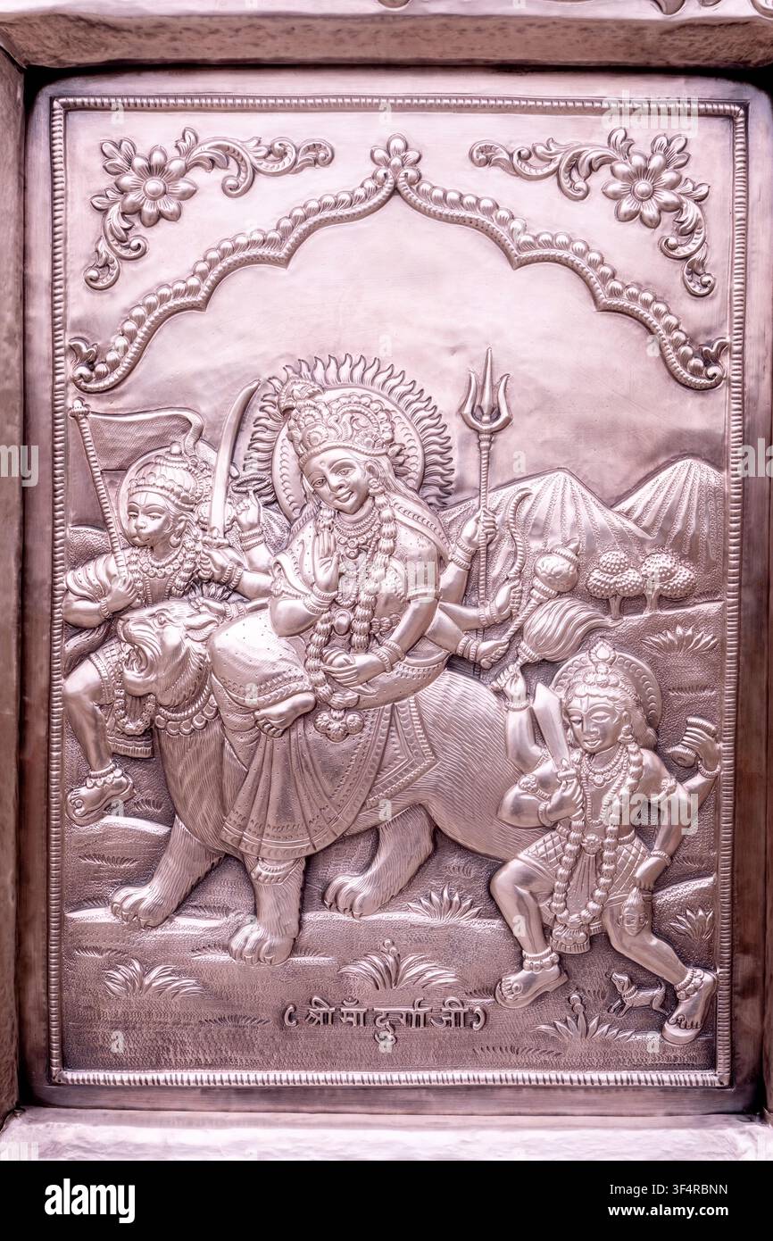 Una scultura in metallo placcato argento che raffigura la dea Durga in sella al suo leone, accompagnata da figure umane e attributi divini, su uno sfondo montuoso Foto Stock