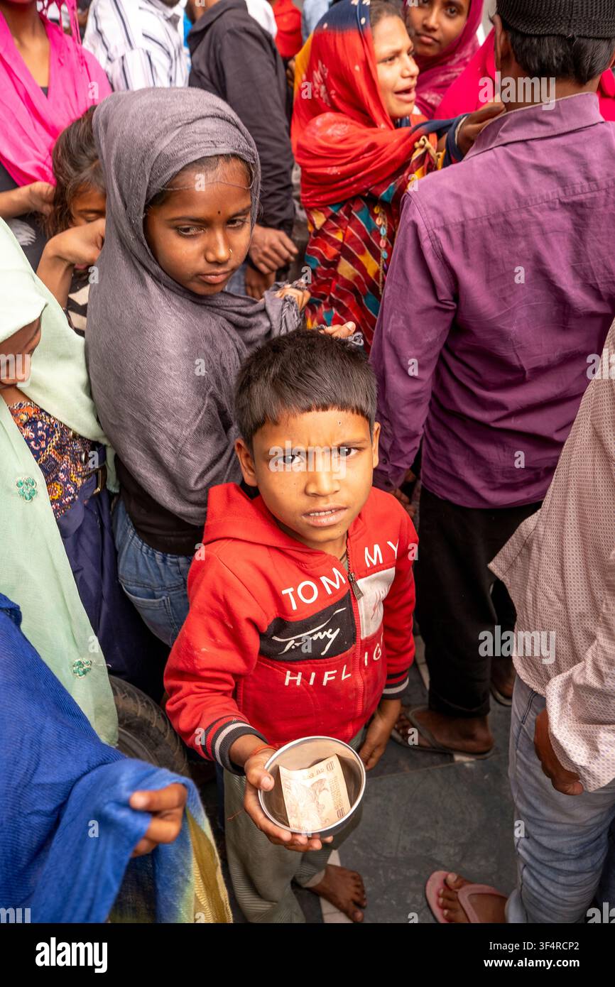 Un bambino porge una ciotola contenente denaro per le elemosine davanti alla moschea Jama Masjid Khairuddin ad Amritsar, Punjab, India. Foto Stock