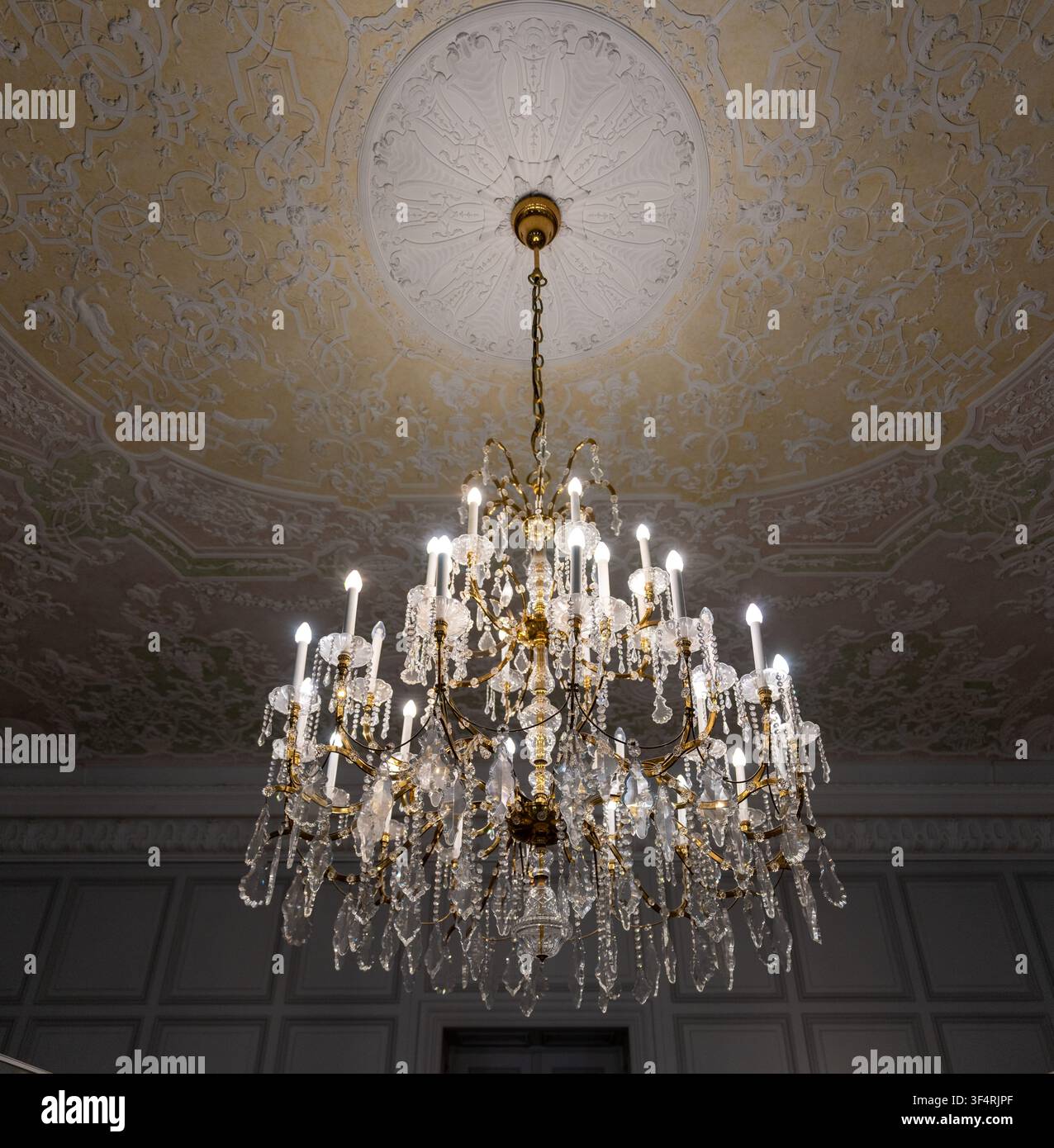 Candelabro di cristallo illuminato sospeso sotto un soffitto rococò ornato all'interno del palazzo barocco di Mannheim a Mannheim, Baden-Württemberg, Germania. Foto Stock