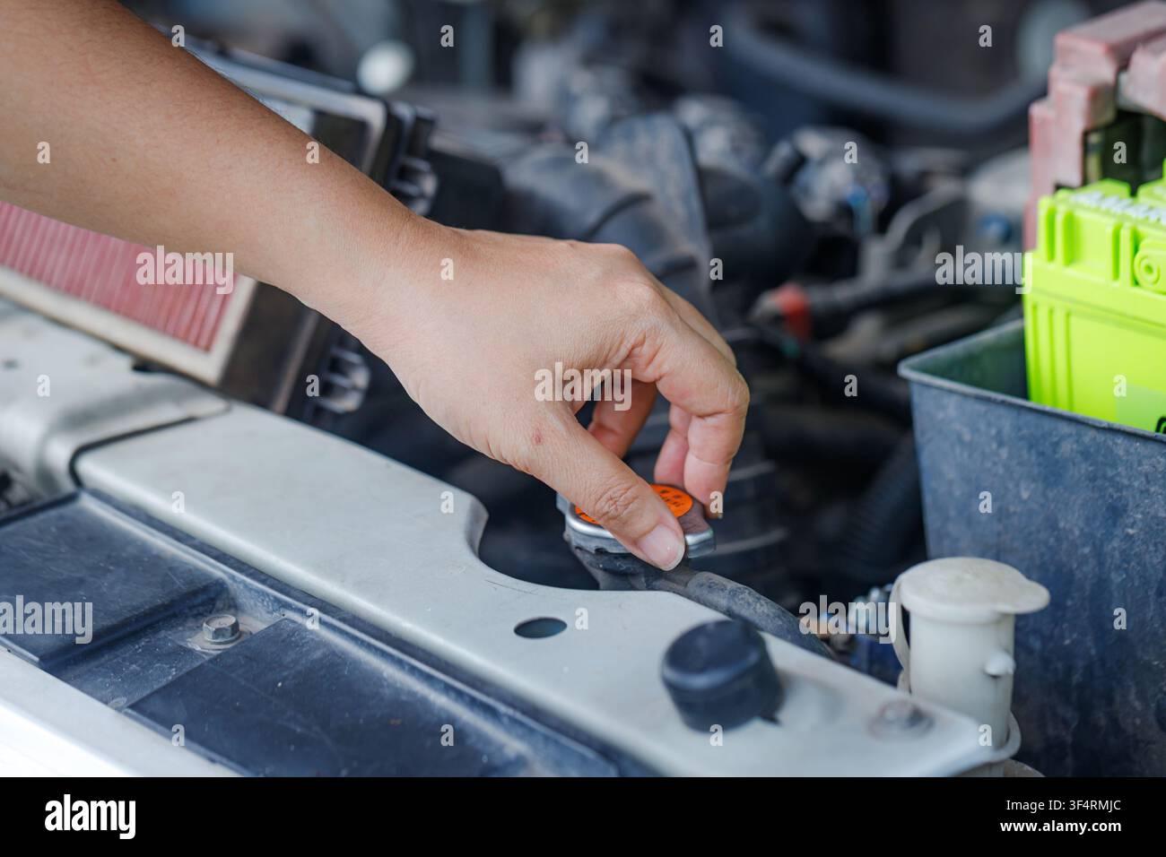 Prima vista di una mano di donna che apre il coperchio della coppa dell'olio motore per controllare il livello dell'olio, evidenziando la manutenzione del veicolo e la cura del motore in un ambiente di officina Foto Stock
