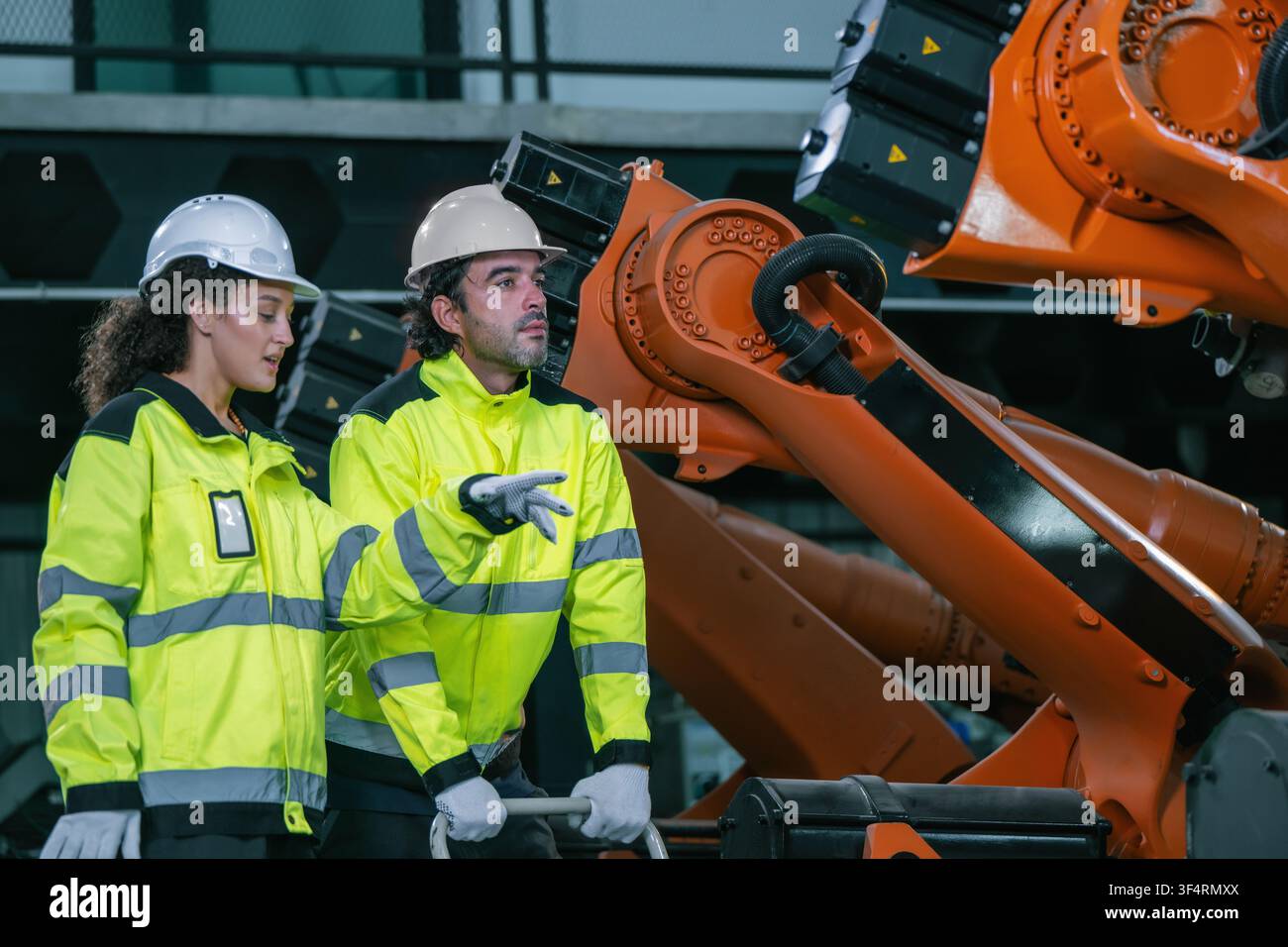 Discussione di squadra di ingegneri industriali sulla manutenzione del braccio robotico in un magazzino di fabbrica. Concetto di servizio di manutenzione di macchinari industriali pesanti, attrezzature Foto Stock
