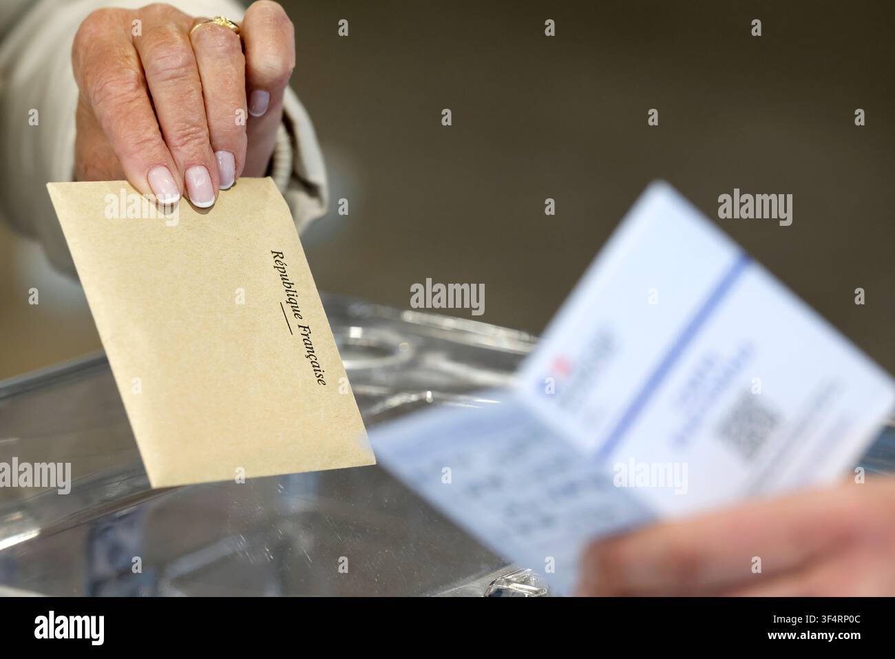 Un elettore deposita la sua busta per il voto, timbrata "Repubblica francese", in un'urna trasparente per le votazioni. Foto Stock