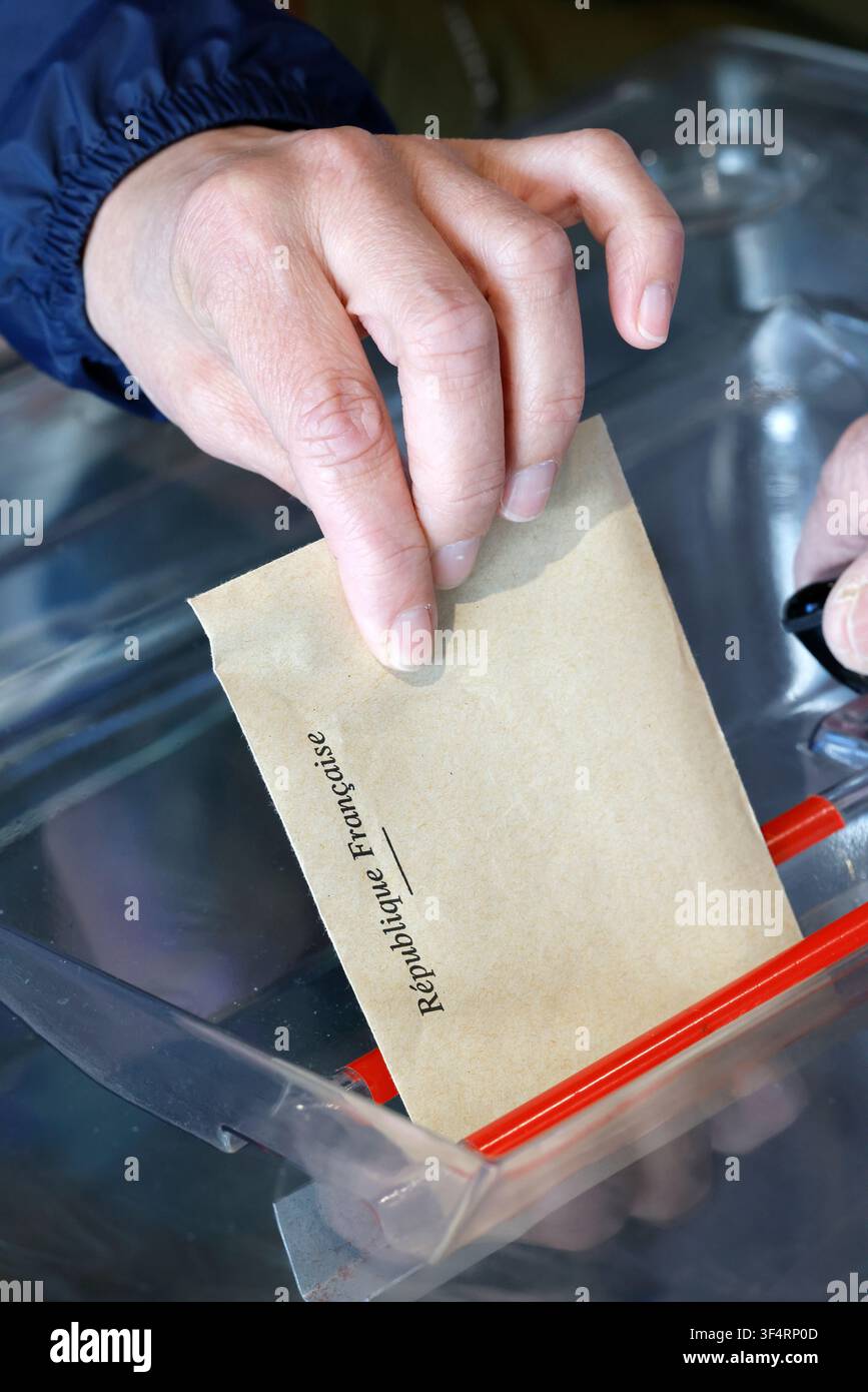 Un elettore che inserisce una busta per il voto in un'urna trasparente durante un'elezione francese. Foto Stock