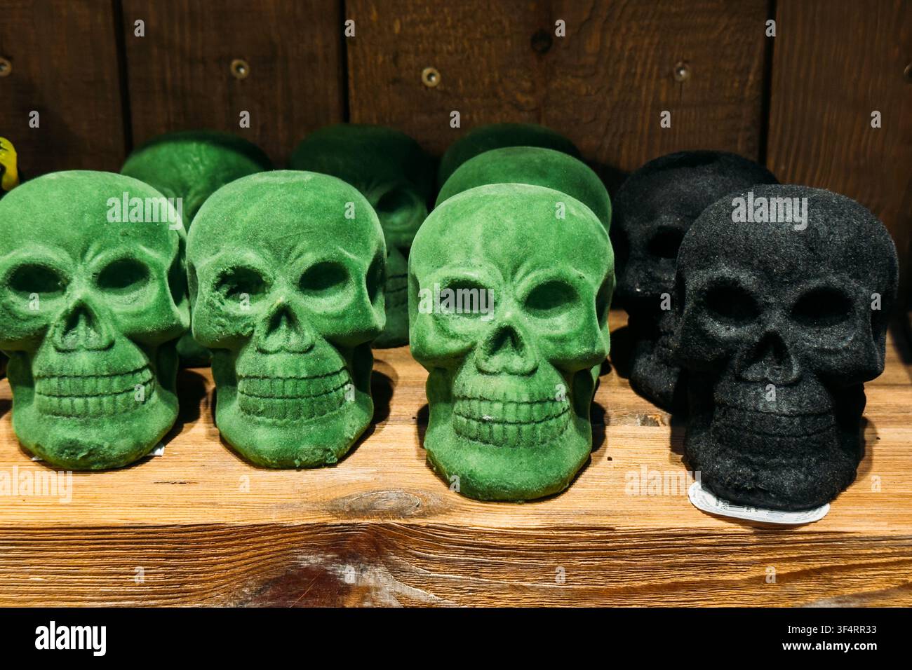 Diverse decorazioni a forma di teschio in velluto verde e nero sono esposte su una mensola di legno. Decorazione gotica, estetica oscura, dettagli spettrali per la casa, Halloween Foto Stock