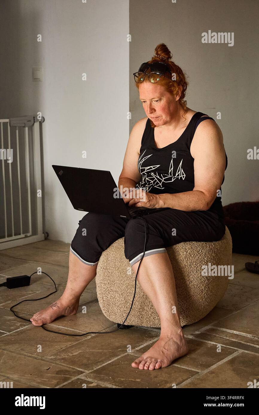 Una donna dai capelli rossi che lavora su un laptop da casa Foto Stock