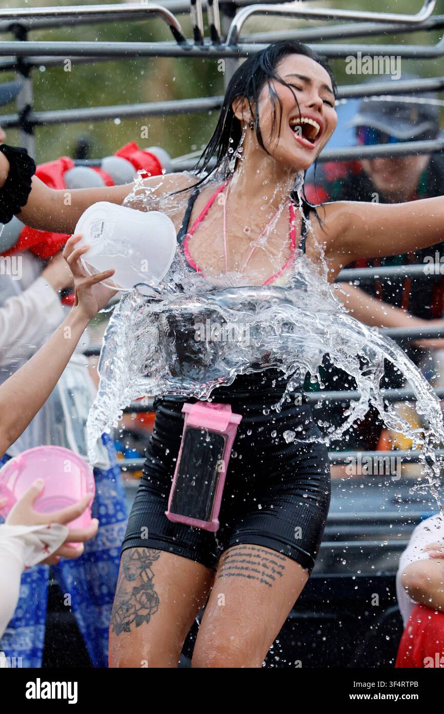 Una giovane donna raggiante di gioia partecipa ai festeggiamenti del Capodanno thailandese, Songkran, mentre viene innaffiata con acqua rinfrescante durante questa tradizione c Foto Stock