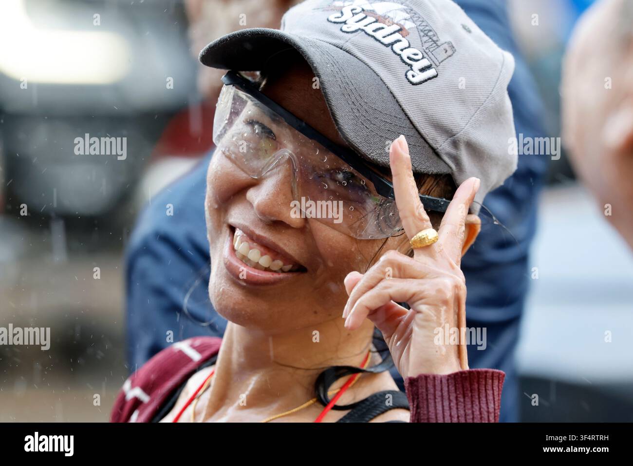 Una donna sorridente che indossa occhiali protettivi e un cappello celebra il festival di Songkran. Gli schizzi d'acqua e la pioggia contribuiscono all'atmosfera festosa di questo T Foto Stock