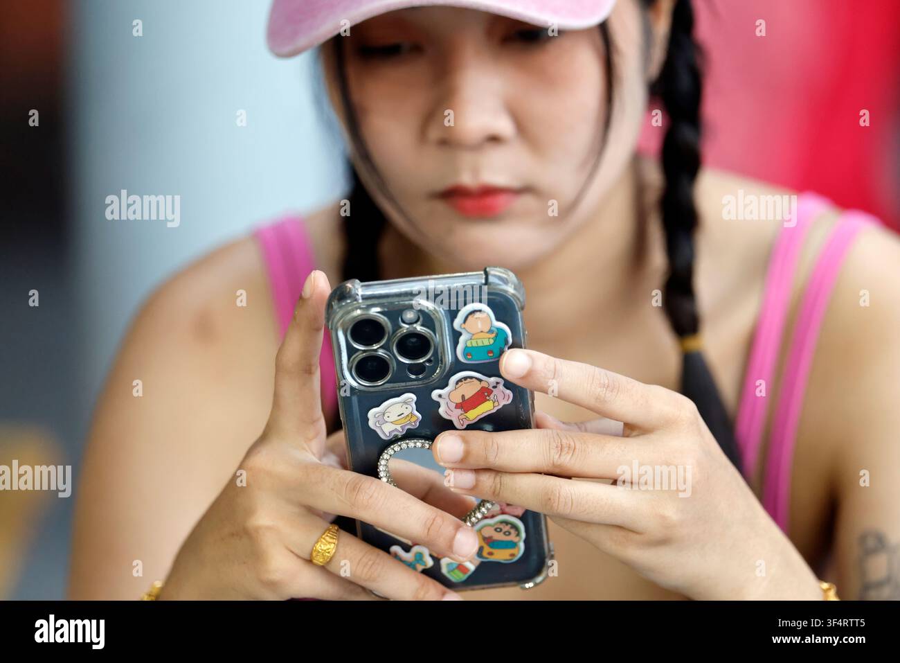 Una giovane donna con i capelli intrecciati sta usando il suo smartphone, decorato con adesivi di personaggi dei cartoni animati. Social media. Pattaya, Thailandia. Foto Stock