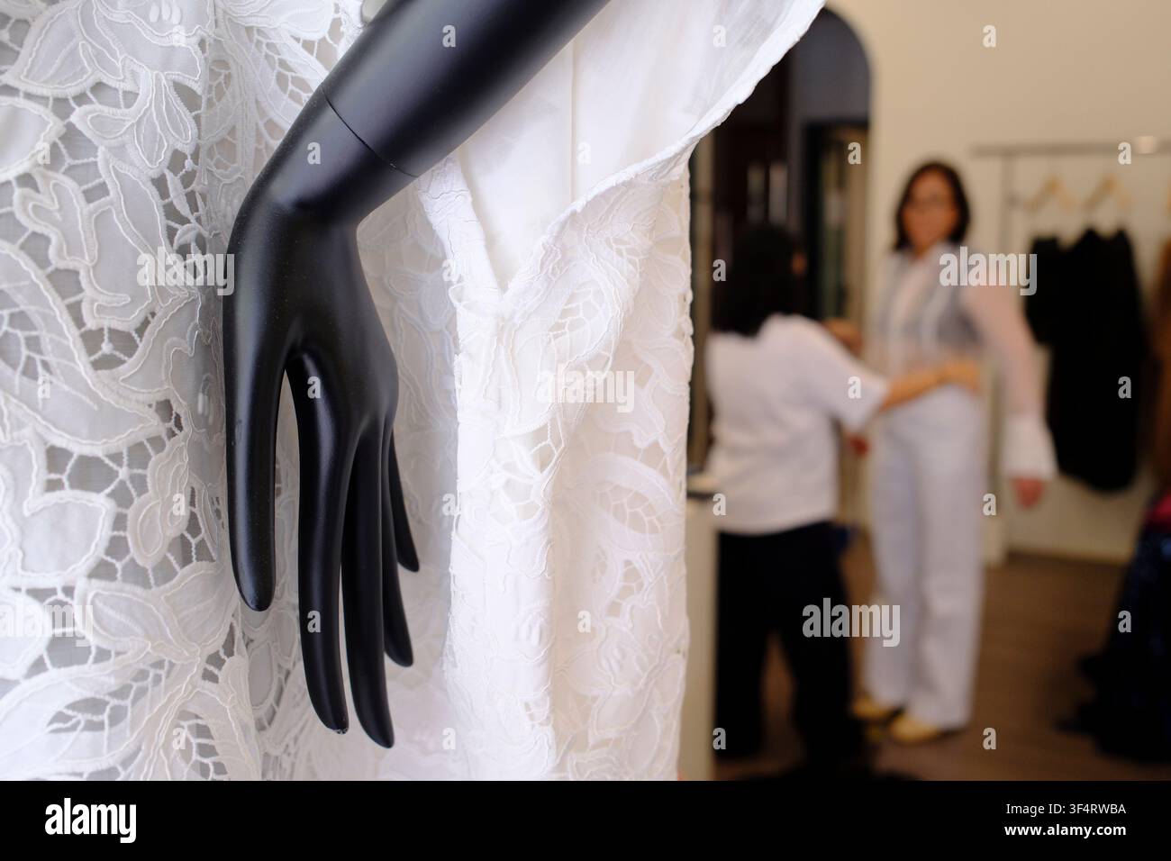 Una modella nera sfila un vestito di pizzo bianco in una sartoria. Una cliente prova un paio di pantaloni bianchi, assistita da una sarta. Ho Chi Minh City, V Foto Stock