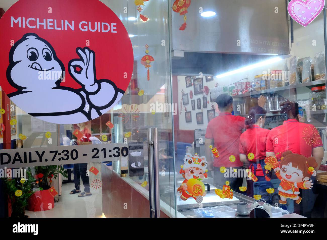 Vetrina di un ristorante con il logo della Guida Michelin e decorazioni per il Capodanno cinese, con il personale in uniformi rosse visibile all'interno. Ho Chi Minh Foto Stock