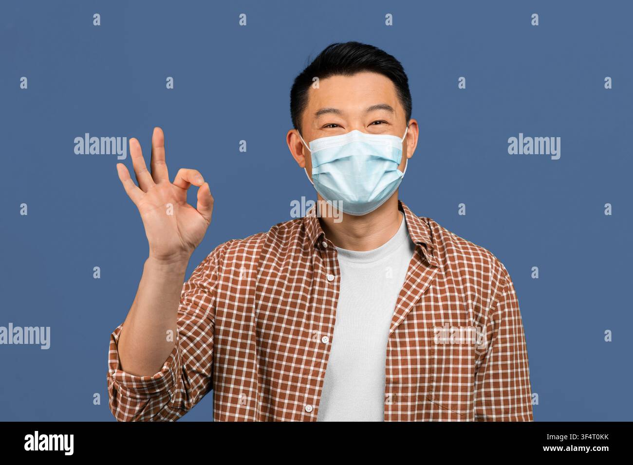 Uomo asiatico sorridente con mascherina che fa il segno dell'ok con la mano, concetto di assistenza sanitaria Foto Stock