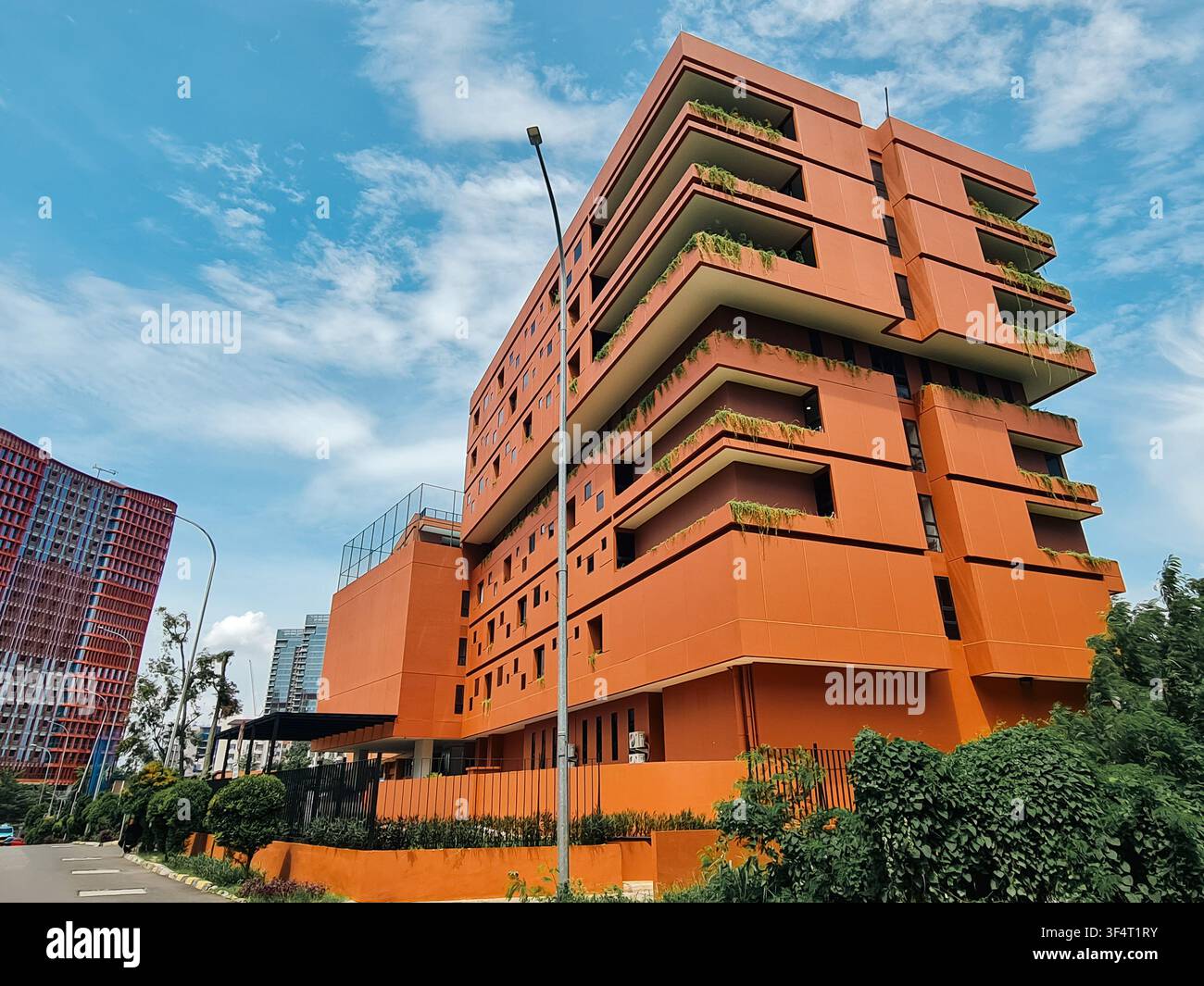 Vista ad angolo basso di un edificio arancione vivace con balconi sporgenti e vegetazione rigogliosa contro un cielo luminoso. Foto Stock