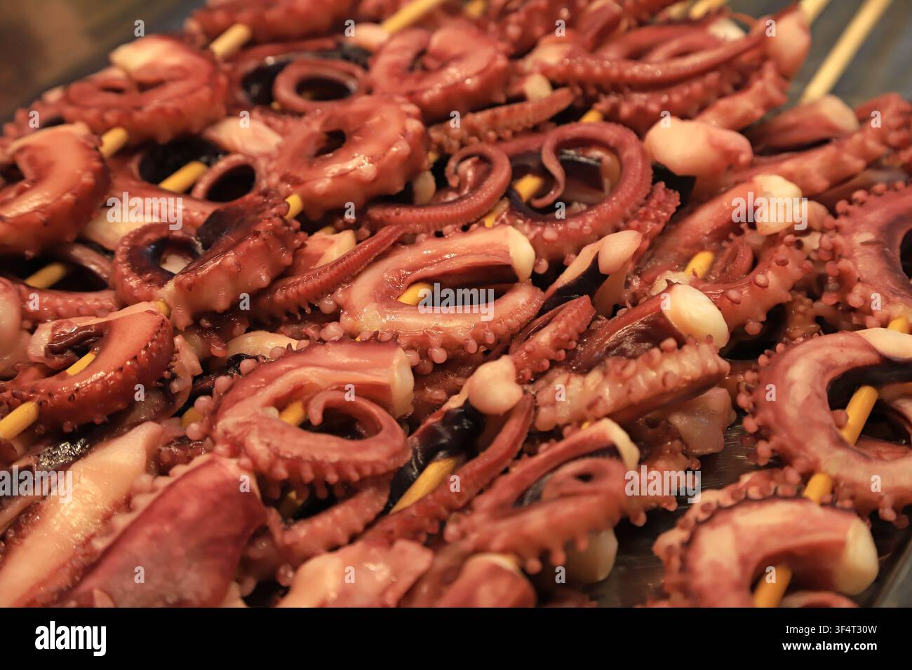 Una vista ravvicinata di succosi tentacoli di polpo infilati su spiedini di legno e grigliati su carboni ardenti. Il pesce rosso-brunastro luccica di olio, sh Foto Stock