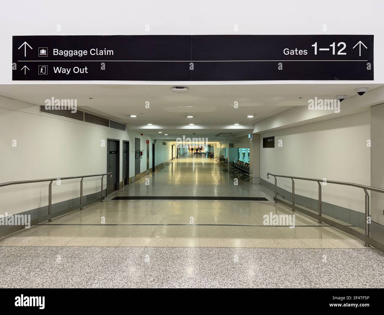 Un corridoio vuoto dell'aeroporto conduce verso il ritiro bagagli sotto i cartelli di orientamento sospesi. Foto Stock
