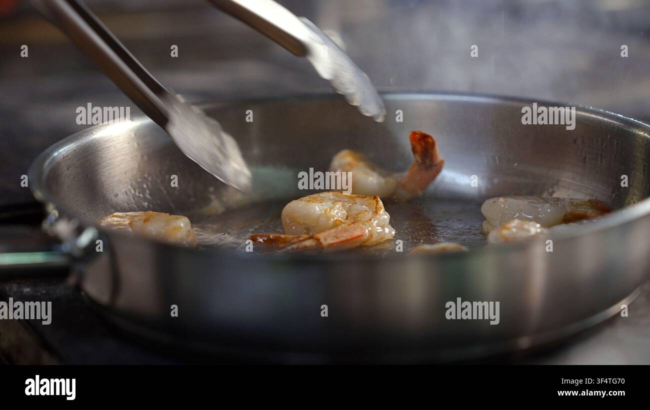 Gamberetti che vengono saltati in una padella con le pinze Foto Stock