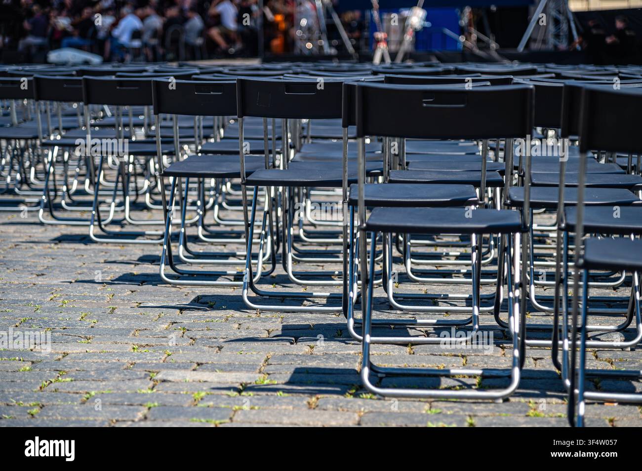 Le sedie sono allineate su una superficie di pietra a Praga per un evento, persone si radunano sullo sfondo. Foto Stock