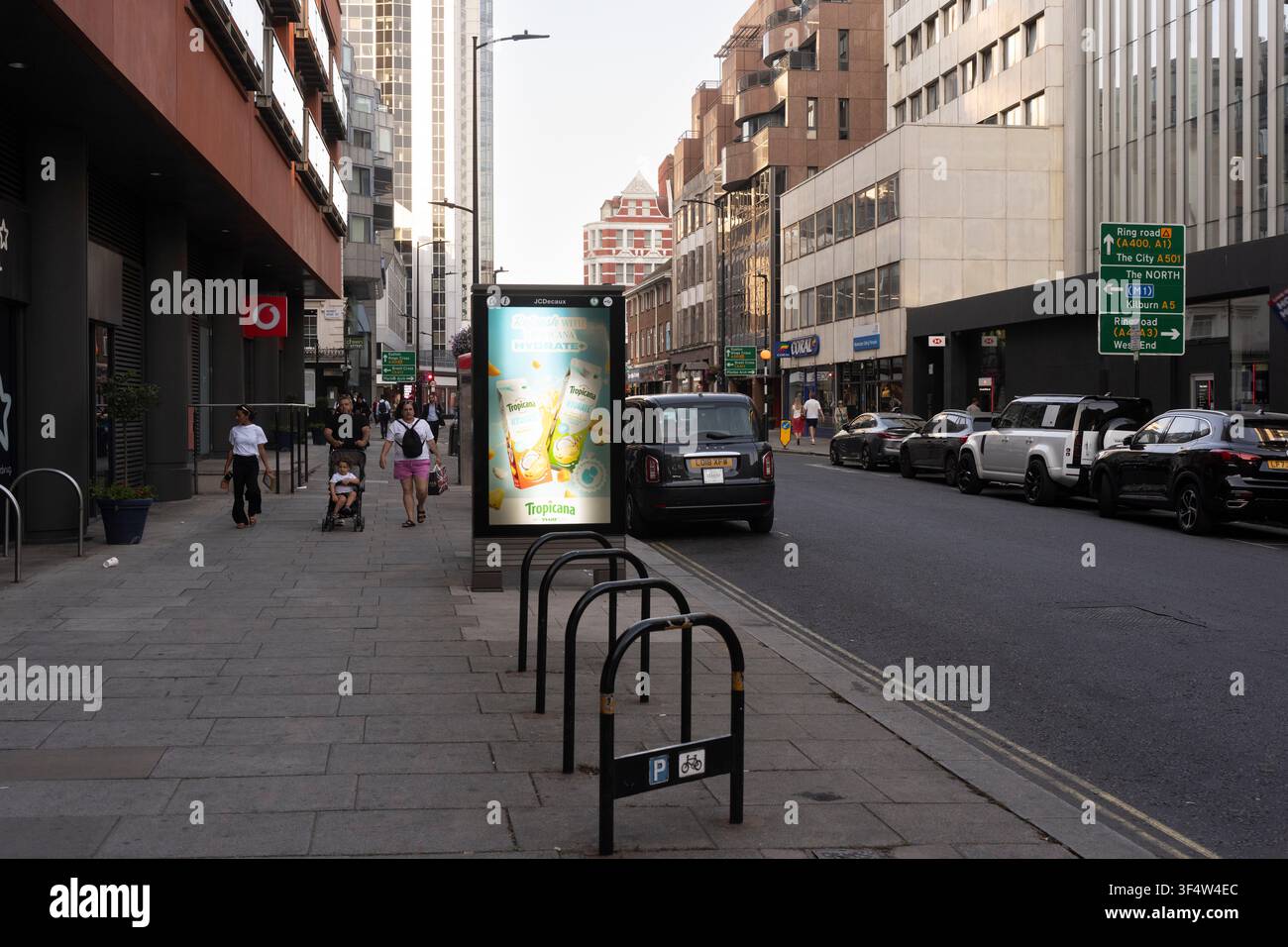 I pedoni passano davanti a un cartellone pubblicitario di Tropicana Hydrate+ su Praed Street a Londra, dove i marchi pubblicizzano per raggiungere il forte traffico pedonale della città. Foto Stock