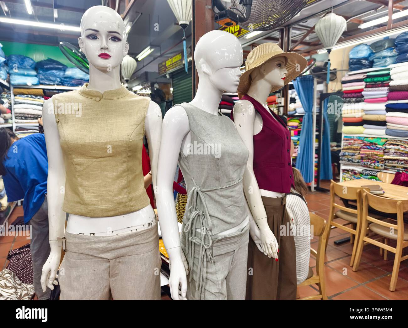Bancarella di mercato di tessuti e sartoria a Hoi An, Vietnam, con manichini che sfoggiano set su misura di lino e di top senza maniche con pantaloni Foto Stock