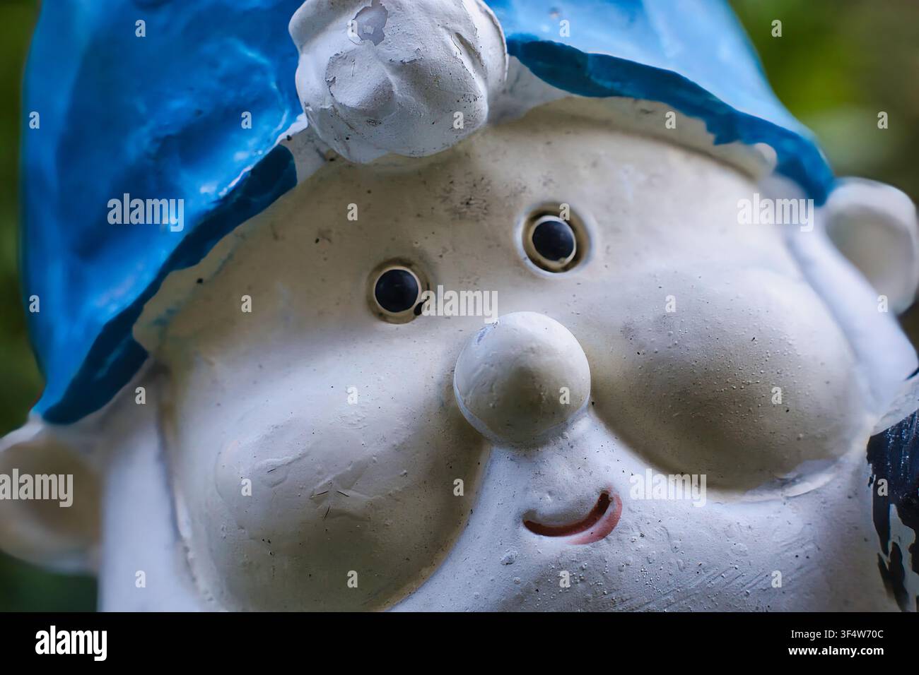 Una fotografia ravvicinata di una statua allegra di gnomo da giardino che indossa un cappello a punta blu brillante. Foto Stock