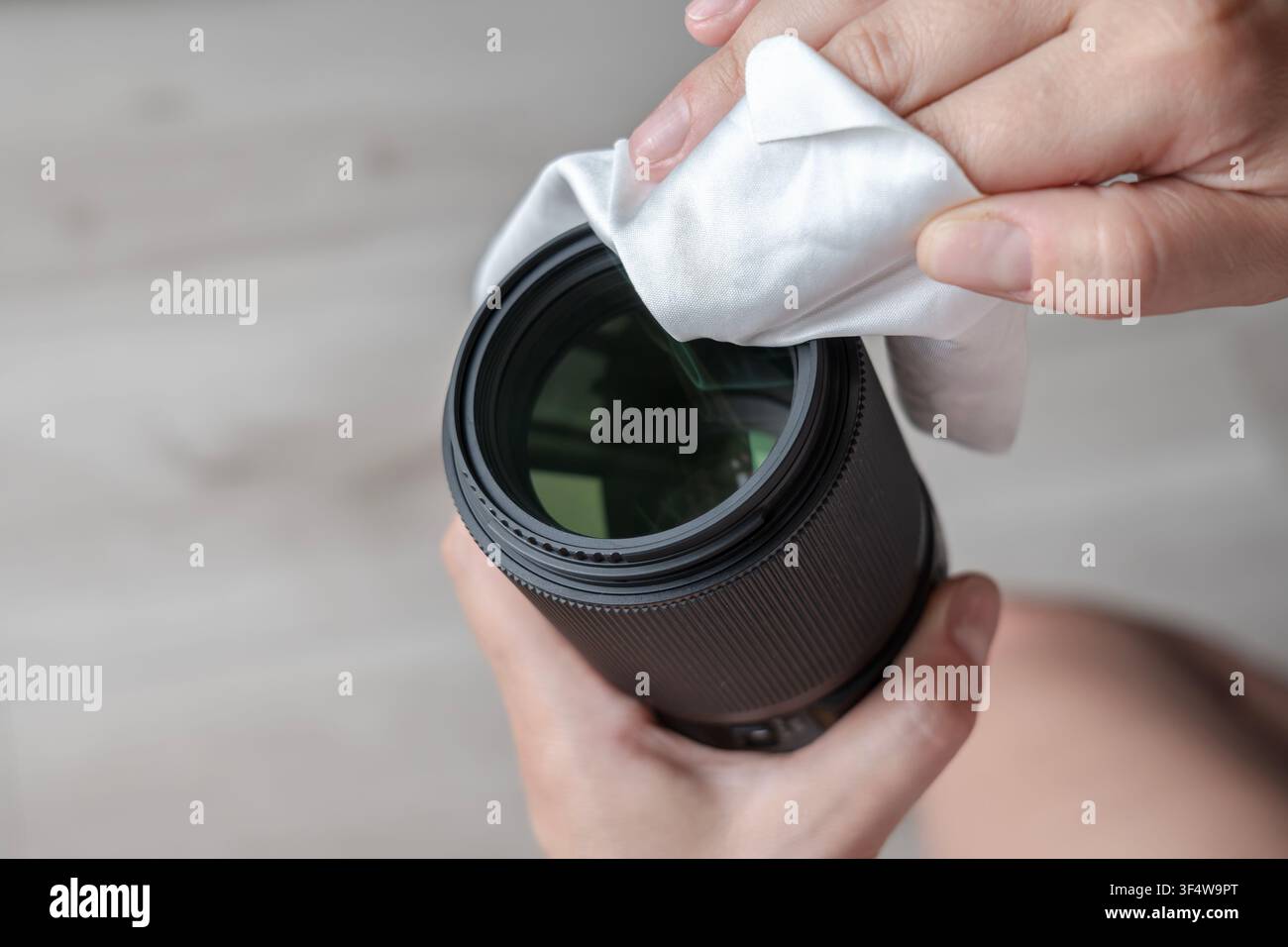 Mani che puliscono meticolosamente una superficie della lente di una fotocamera digitale con un panno specializzato Foto Stock